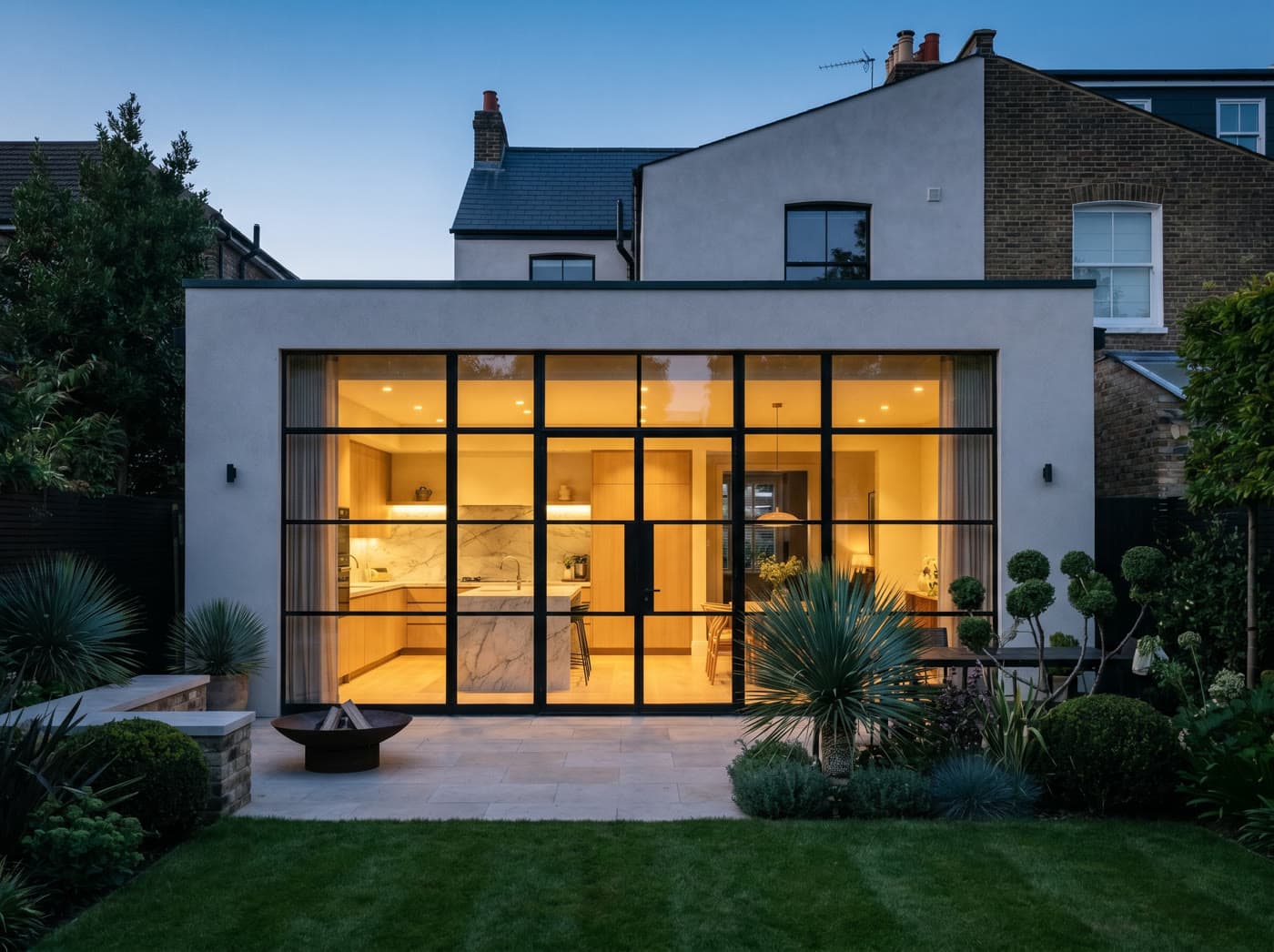 A completed rear house extension at dusk, glowing warm from the kitchen inside